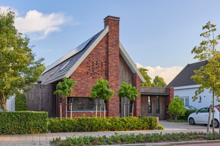 Moderne bakstenen woning met puntdak, zonnepanelen en groene voortuin in rustige woonwijk