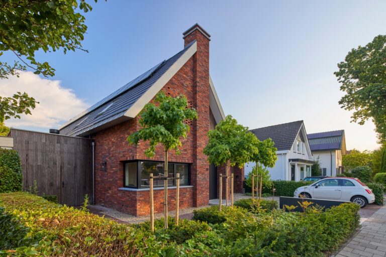 Moderne bakstenen woning met puntdak, zonnepanelen en groene voortuin in rustige woonwijk