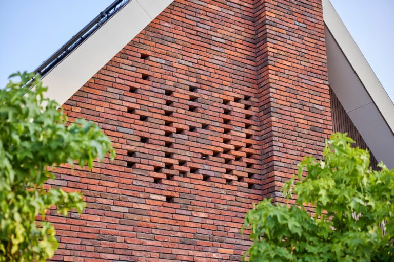 Moderne bakstenen woning met puntdak, zonnepanelen en groene voortuin in rustige woonwijk