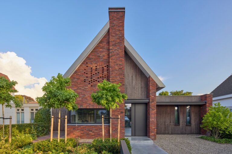Moderne bakstenen woning met puntdak, zonnepanelen en groene voortuin in rustige woonwijk