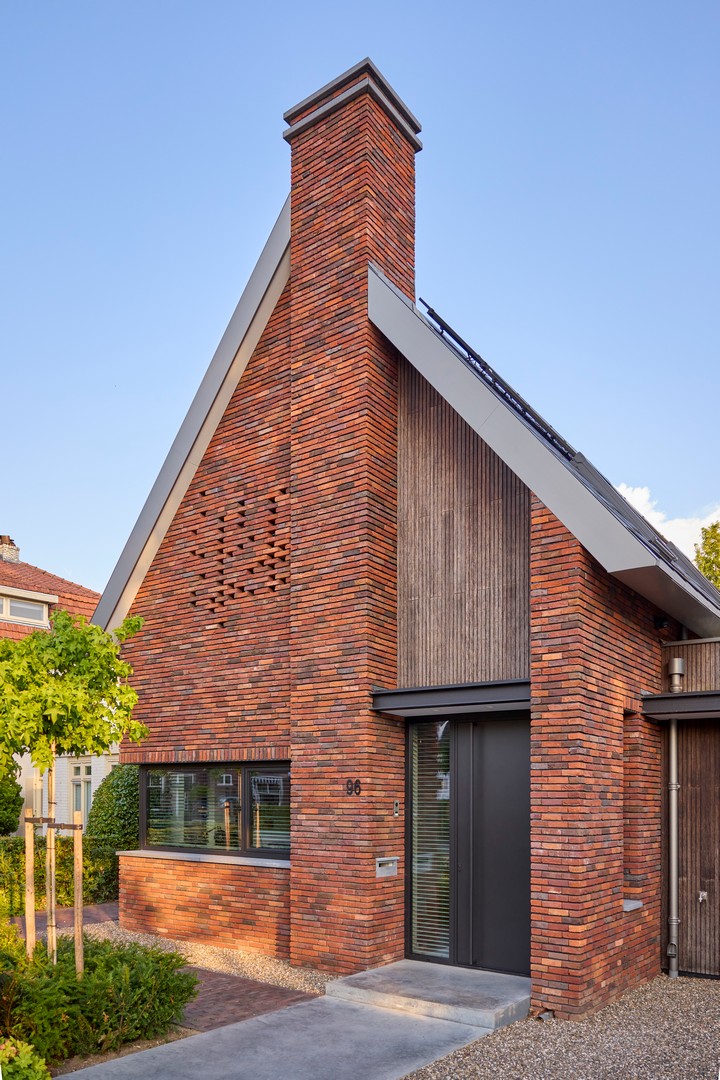 Moderne bakstenen woning met puntdak, zonnepanelen en groene voortuin in rustige woonwijk