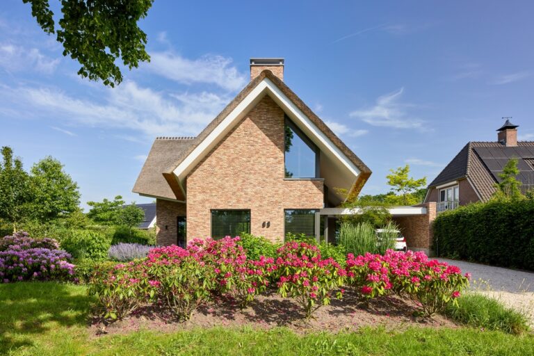 Voorgevel van een landelijke woning met rieten dak en kleurrijke bloementuin