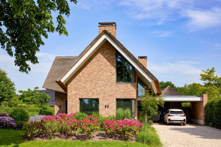 Vrijstaande landelijke woning met rieten dak, carport en bloeiende voortuin