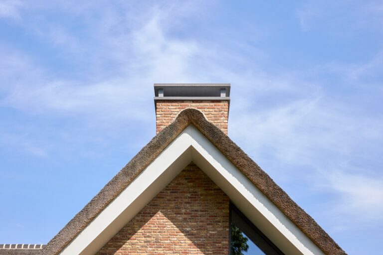 Detail van de hoge bakstenen topgevel met rieten dak en schoorsteen