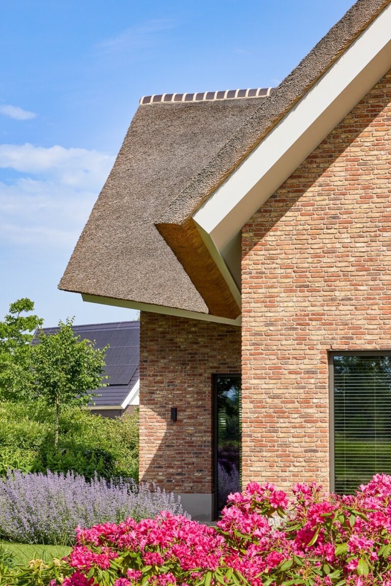 Detail van het rieten dak, de bakstenen gevel en kleurrijke tuinbeplanting