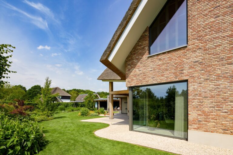 Grote glazen pui in een landelijke bakstenen woning met aangelegde tuin