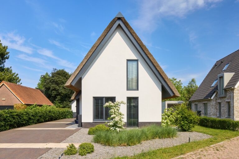 Vooraanzicht van een moderne rietgedekte villa met wit gestucte gevel en eigentijdse architectuur.