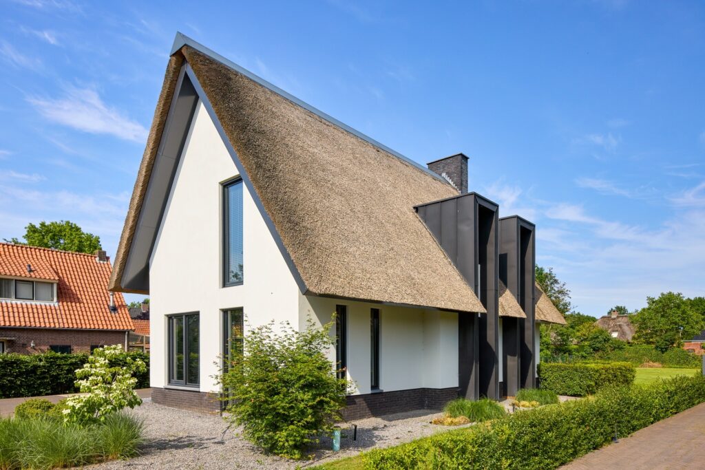 Zijaanzicht van een exclusieve rietgedekte villa met karakteristieke dakkapellen en moderne details.