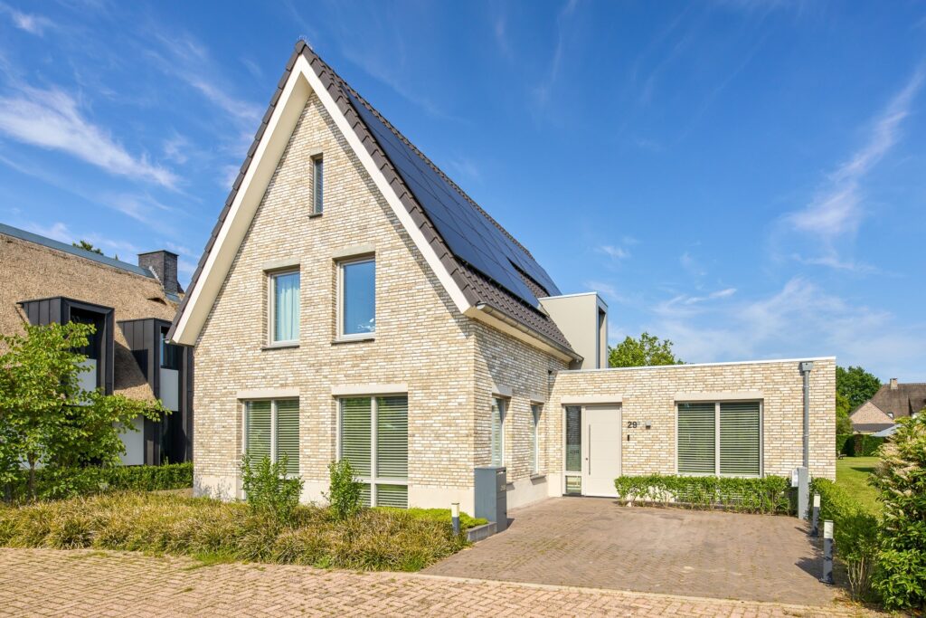 Voorgevel van een moderne woning met lichte baksteen, grote raampartijen en eigentijds ontwerp.