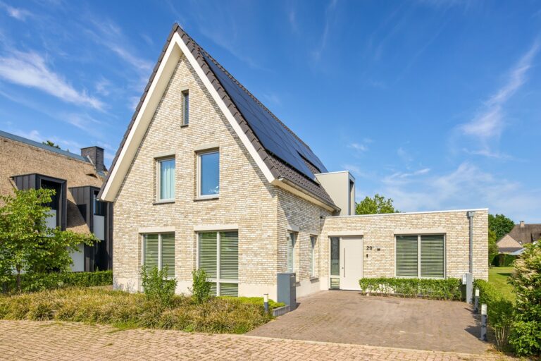 Voorgevel van een moderne woning met lichte baksteen, grote raampartijen en eigentijds ontwerp.