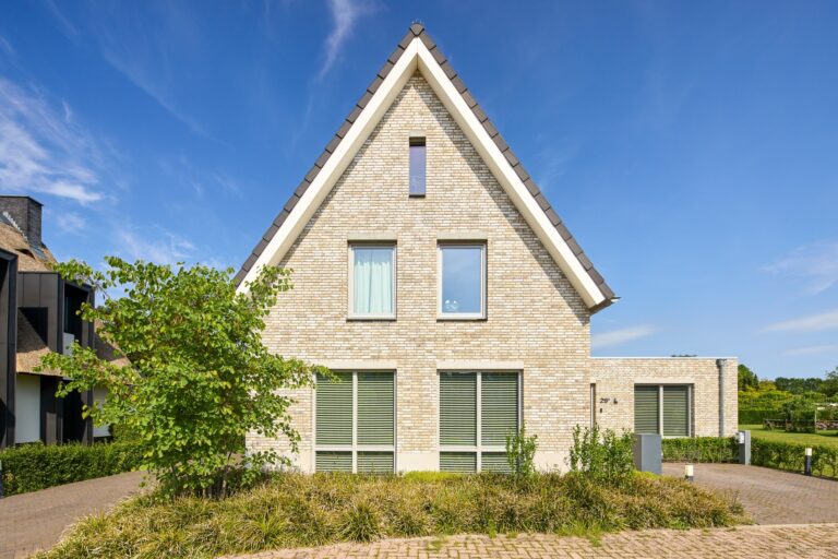 Moderne rietgedekte villa met wit gestucte gevel en luxe architectuur in een groene woonomgeving.