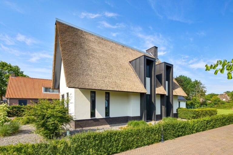 Donkere vrijstaande woning met markante entree, hoge glaspartij en moderne architectuur.