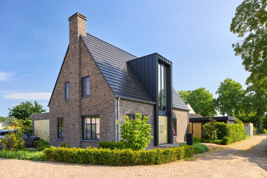 Moderne villa met donkere baksteen, hoge entree en luxe architectuur in een groene woonwijk
