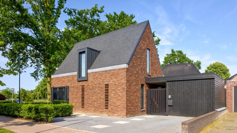 Eigentijdse woning waarin warme baksteen, een markante kap en donkere houten details samenkomen in een krachtig en sfeervol ontwerp.