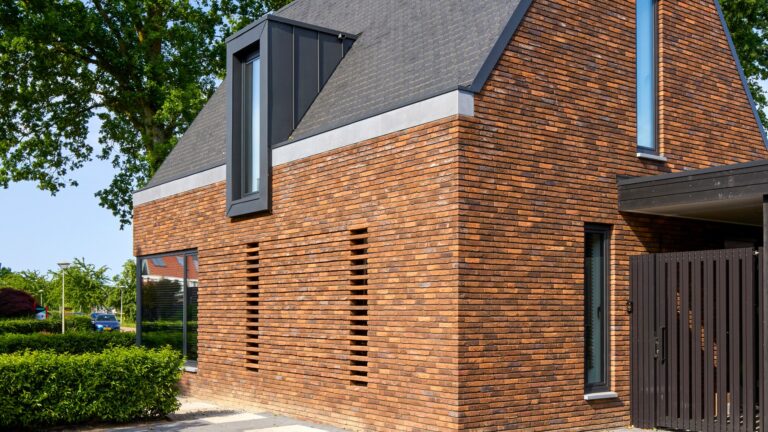 Eigentijdse woning waarin warme baksteen, een markante kap en donkere houten details samenkomen in een krachtig en sfeervol ontwerp.