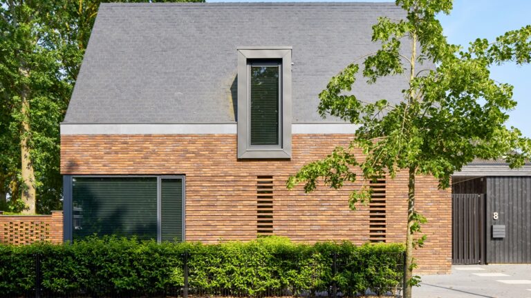 Eigentijdse woning waarin warme baksteen, een markante kap en donkere houten details samenkomen in een krachtig en sfeervol ontwerp.
