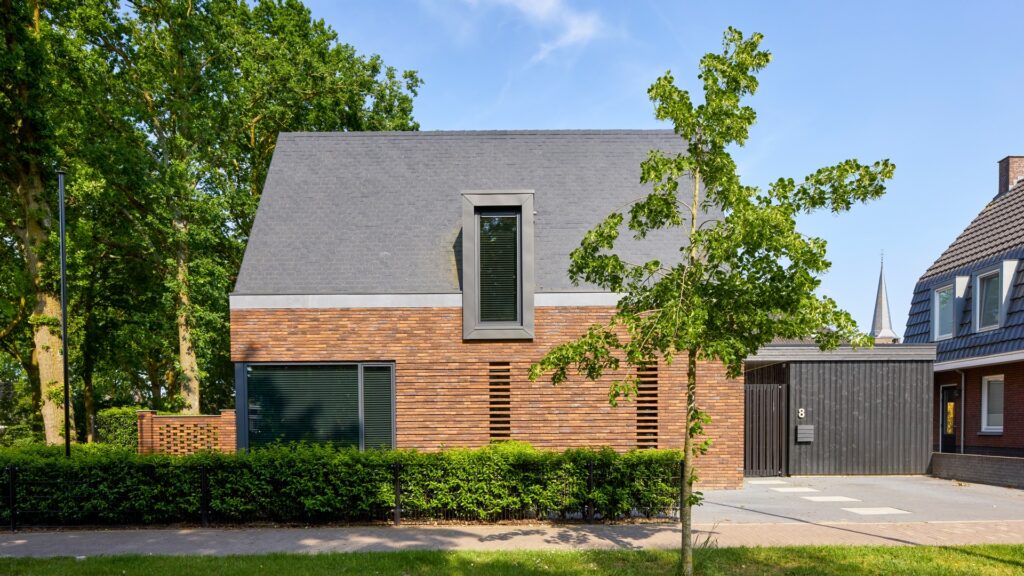 Eigentijdse woning waarin warme baksteen, een markante kap en donkere houten details samenkomen in een krachtig en sfeervol ontwerp.