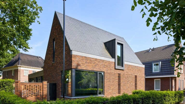 Eigentijdse woning waarin warme baksteen, een markante kap en donkere houten details samenkomen in een krachtig en sfeervol ontwerp.