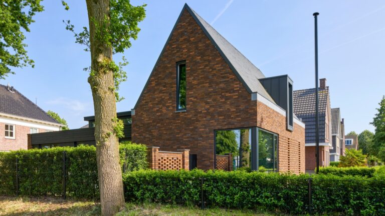 Eigentijdse woning waarin warme baksteen, een markante kap en donkere houten details samenkomen in een krachtig en sfeervol ontwerp.