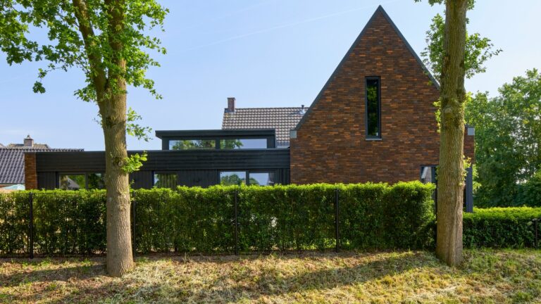 Eigentijdse woning waarin warme baksteen, een markante kap en donkere houten details samenkomen in een krachtig en sfeervol ontwerp.