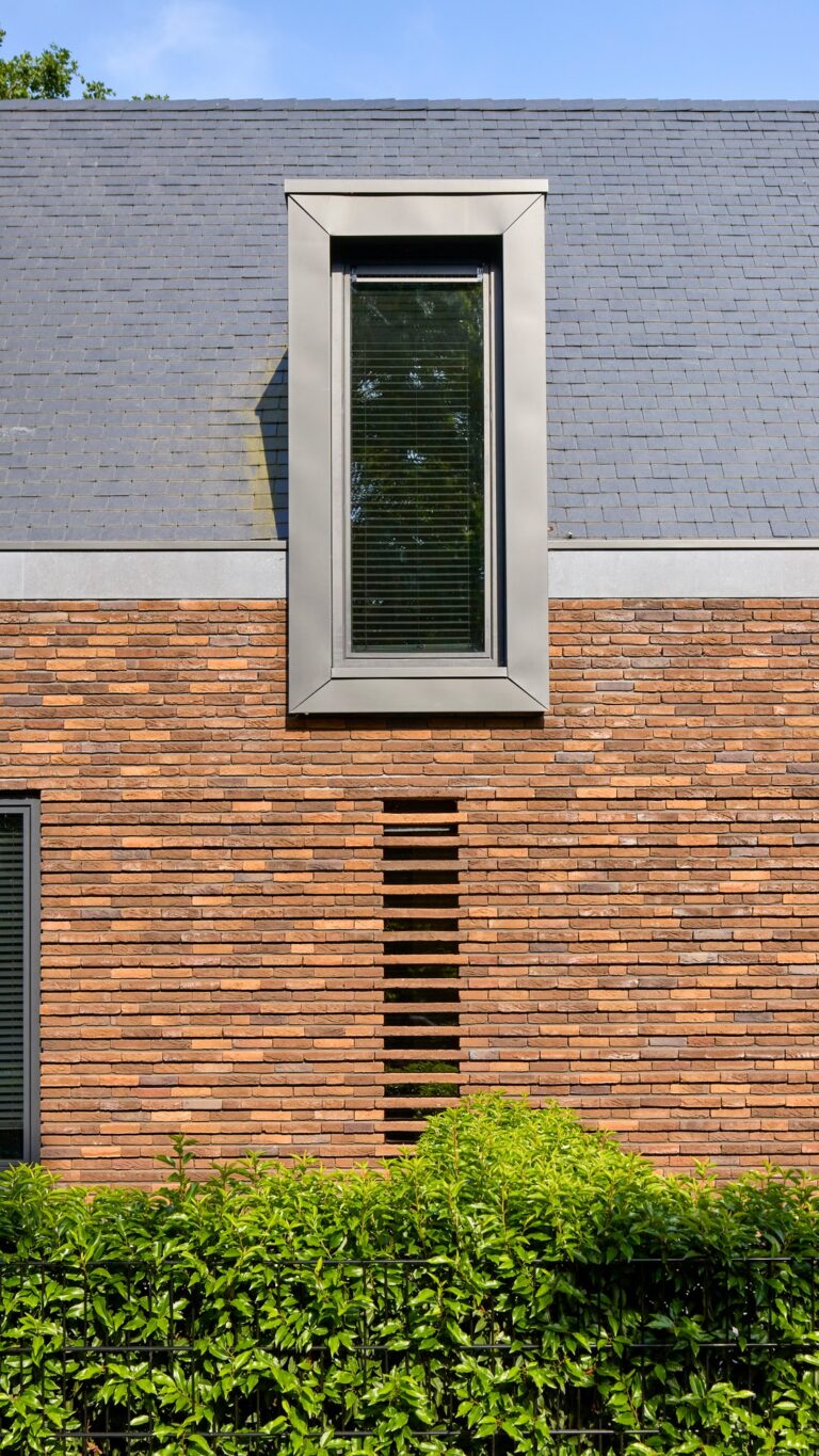Eigentijdse woning waarin warme baksteen, een markante kap en donkere houten details samenkomen in een krachtig en sfeervol ontwerp.